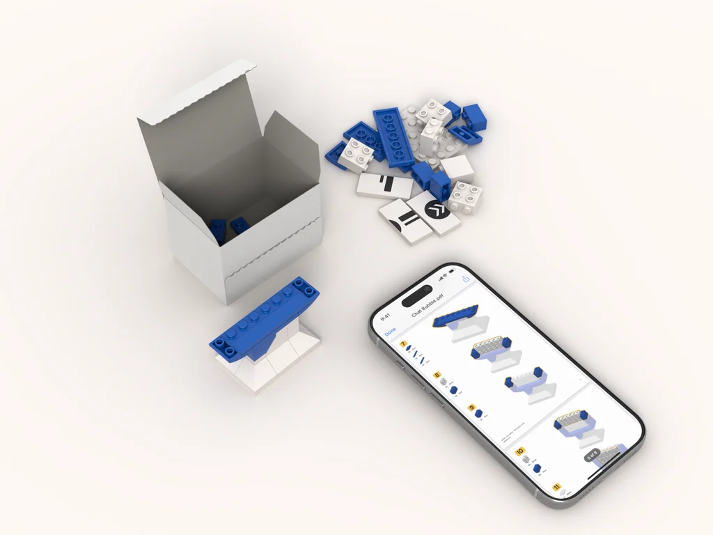 A half-built chat bubble of blue and white bricks beside its open kit box and a small pile of the remaining parts, with a phone showing the instructions open at the next step.