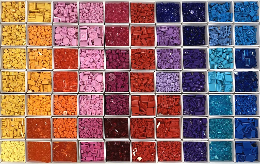 Seen from above, rows of white compartments, each holding one color of sorted parts, running from yellow and orange through pink, red and purple to the blues.